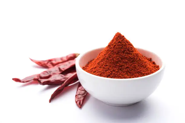 Photo of Red Chilli Powder in a bowl with dried red chillies over colourful background or pile of red chilli powder over plain background