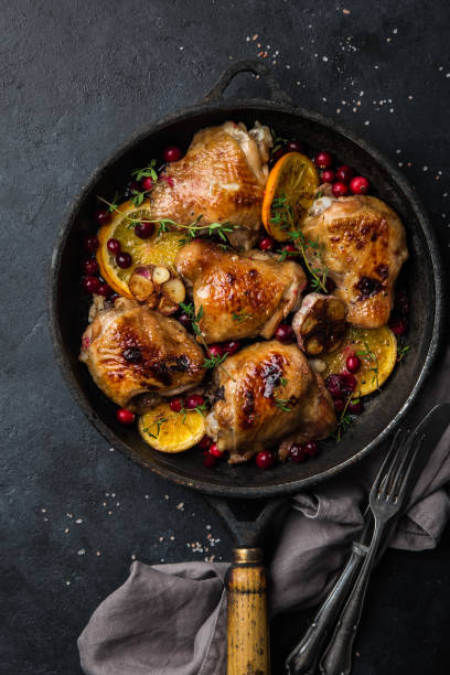 roasted  chicken with orange, cranberry and spicy herbs on pan roasted  chicken with orange, cranberry and spicy herbs on pan , black concrete background, top view, skillet cooking pan photos stock pictures, royalty-free photos & images