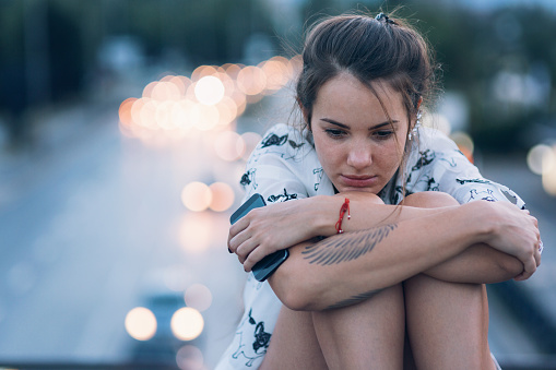 Young beautiful woman sitting on the bridge and looking down in sadness