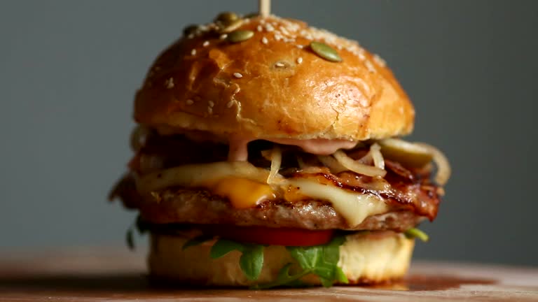 Great Burger with beef cutlet, tomatoes, mushrooms and cucumbers with melted cheese rotates on a wooden Board on light background