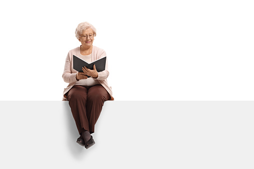 Elderly woman sitting on a panel and reading a book isolated on white background