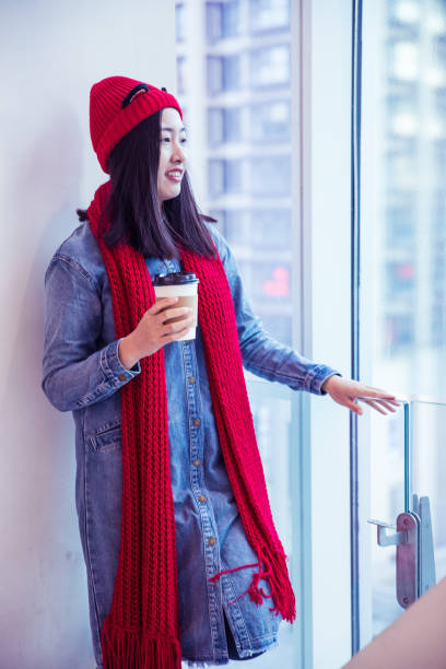 istock Young woman holding coffee by window 894413104