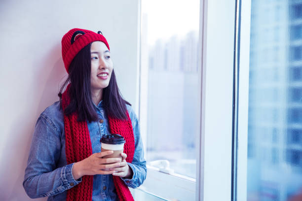 Young woman holding coffee by window