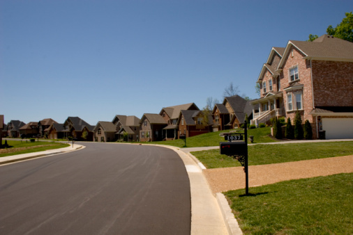 Row of new brick homes in a new subdivision and a street winding through them with a clear blue sky in the background.