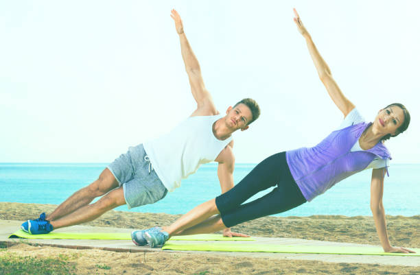 istock Young couple training yoga poses sitting on beach 894446856