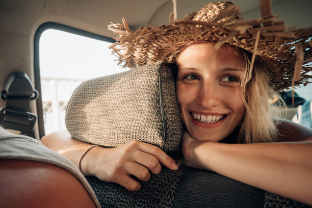 Young backpacker woman wearing a straw hat in the back of a 4x4 car.