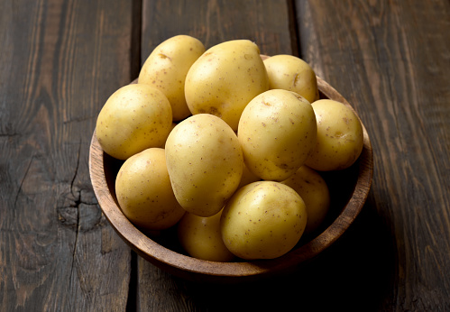 Raw potatoes in bowl on wooden table. Close up view