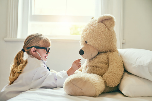 Shot of an adorable little girl dressed up as a doctor and examining a teddy bear with a stethoscope