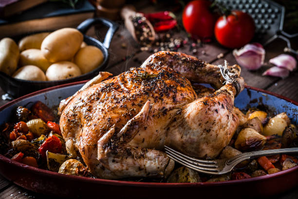 Baked chicken with vegetables on rustic wooden table Horizontal view of a baked chicken with vegetables in an oval baking sheet shot on rustic wooden table. Predominant color is brown. Low key DSRL studio photo taken with Canon EOS 5D Mk II and Canon EF 100mm f/2.8L Macro IS USM comprehensive stock pictures, royalty-free photos & images