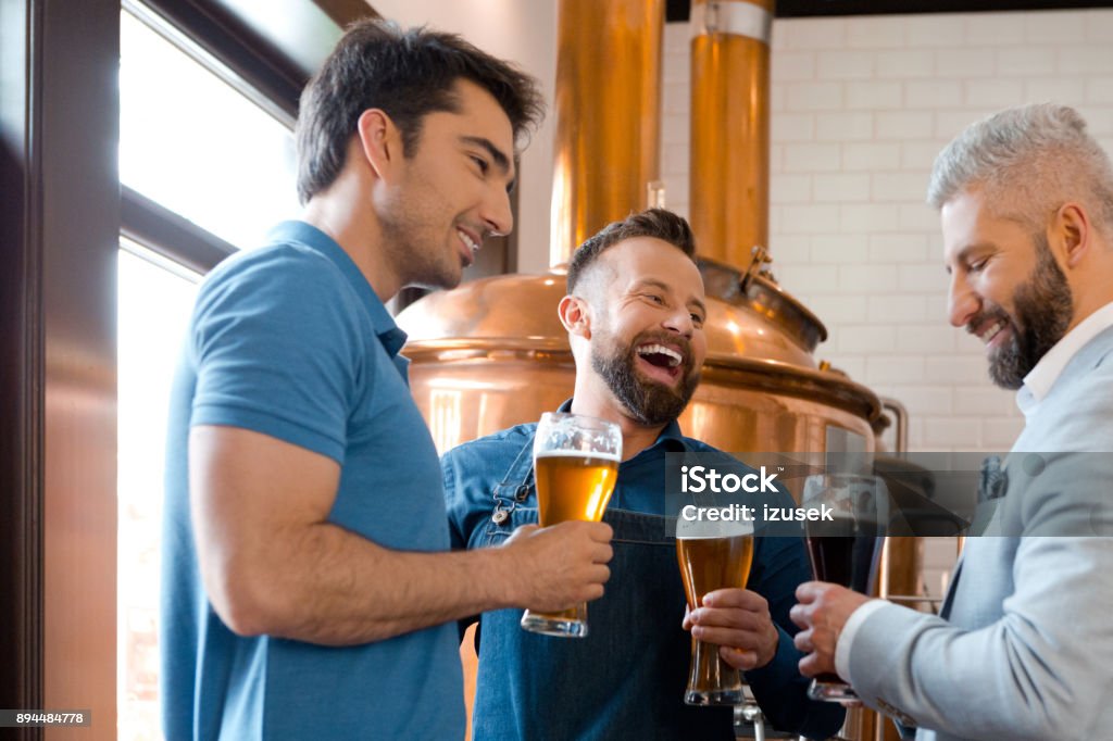 Brewery team having beer after work Microbrewery team having beer after work. Three man drinking beers and smiling at brewery. Brewery Stock Photo