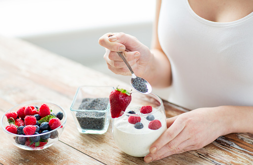 healthy eating, vegetarian food, diet and people concept - close up of woman hands with yogurt, berries and poppy or chia seeds on spoon