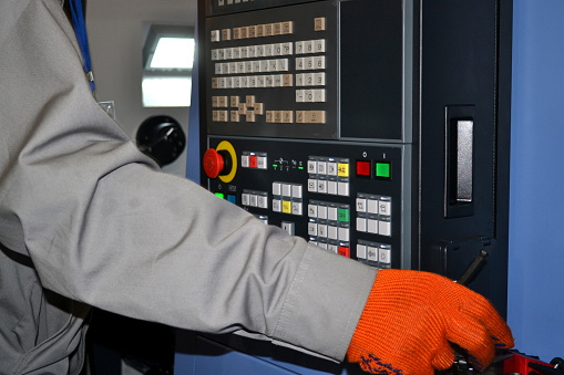 Person works behind the control panel of the production machine at the factory. Industrial production, heavy machinery