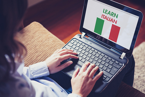 Woman sitting at home with a laptop on the knees and a website to learn Italian on the screen.