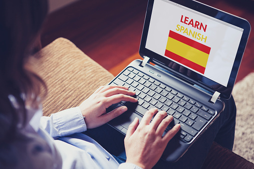 Woman sitting at home with a laptop on the knees and a website to learn Spanish on the screen.