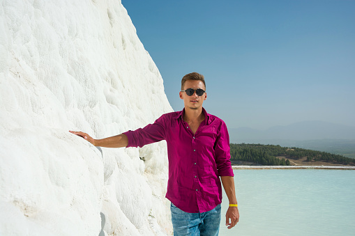 A handsome young man in front of a white mountain background of calcareous sediments and water of travertine in Pamukkale, Turkey.
