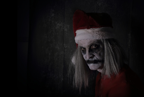 A creepy, evil looking Santa Claus with ghoulish makeup looks menacingly at the camera.