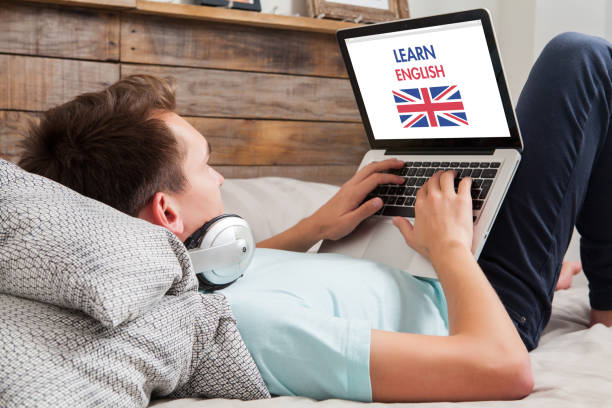 Man learning english at home. Man lying down on the bed at home while uses a laptop to learn English by internet. britain british audio stock pictures, royalty-free photos & images