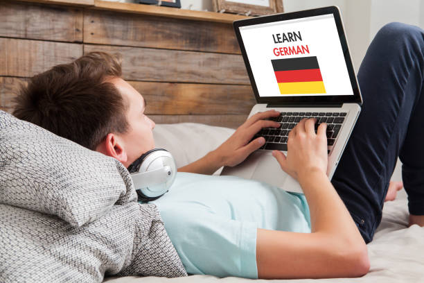 Man learning german at home. Man lying down on the bed at home while uses a laptop to learn German language by internet. german language photos stock pictures, royalty-free photos & images