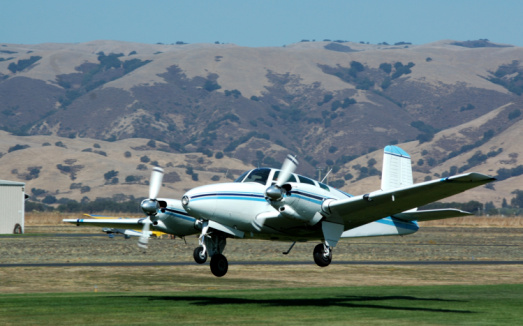 Twin engine airplane taking off on a grass airstrip. Beech Baron.