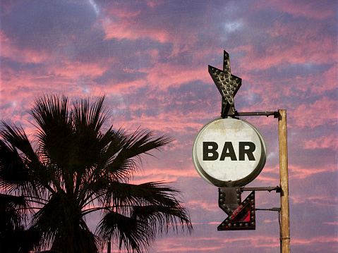aged and worn bar sign at sundet with palm trees