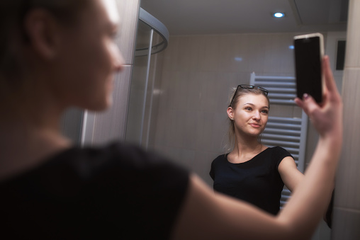 Beautiful Teenage Girl Taking a Selfie in front of a mirror in Bathroom.