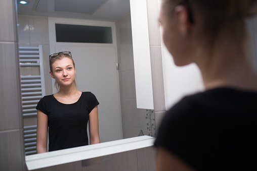 Beautiful Teenage Girl Looking at Herself in Mirror.