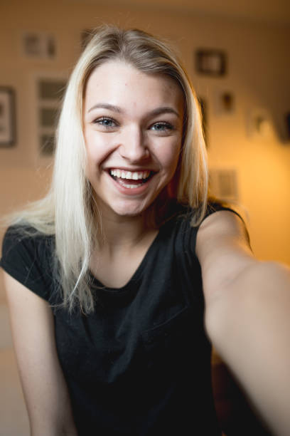 hermosa chica adolescente alegre tomando un selfie en dormitorio - teenage girls pretty smile looking at camera waist up fotografías e imágenes de stock