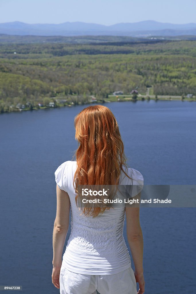 Red-haired girl looking over blue lake Red-haired girl looking over blue lake from the mountain. Women Stock Photo