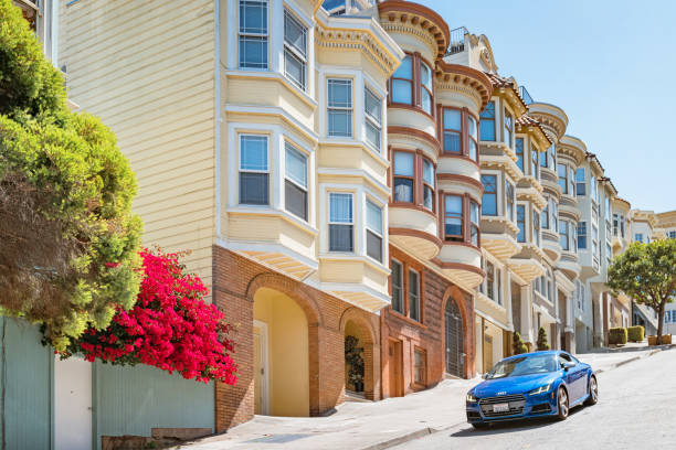 Audi TT drives past ornate townhouses on a steep street in San Francisco, California, USA ona sunny day.