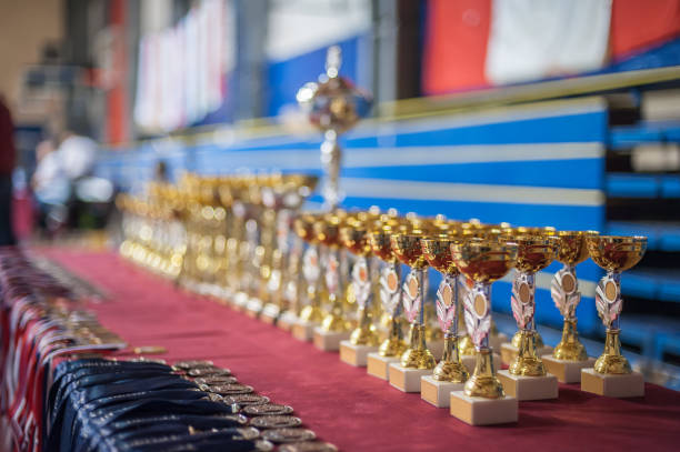 Gold champion trophies and medals lined up in rows. Selective focus