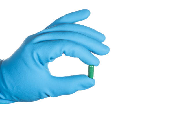 cropped hand of person holding capsule against white background - surgical glove human hand holding capsule imagens e fotografias de stock