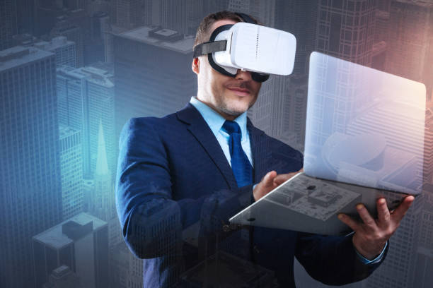 istock Cheerful young man with laptop trying on virtual reality goggles 894730718