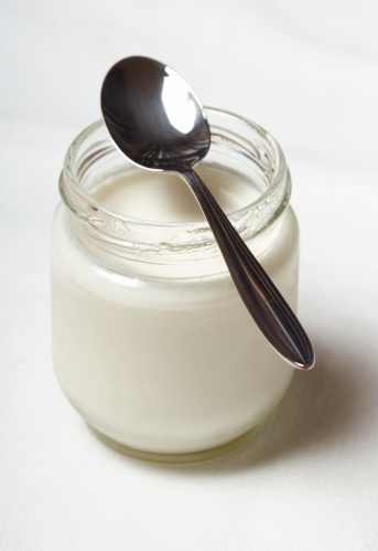 white yogurt in glass jar with spoon over white tablecloth
