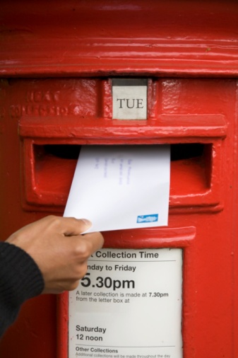 A woman posts a letter in a traditional British red post box