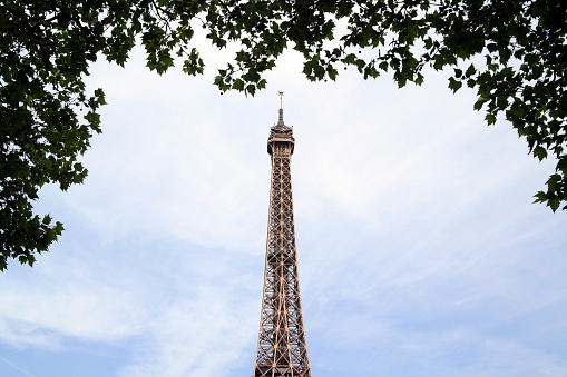 Top of the Eiffel Tower seen between the leaves of trees on a summer day in Paris, France