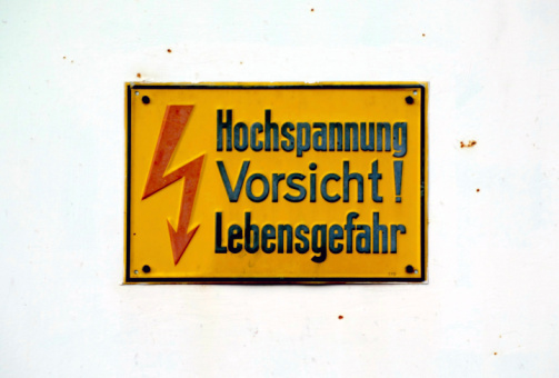 old yellow high voltage sign in German on white rusty background