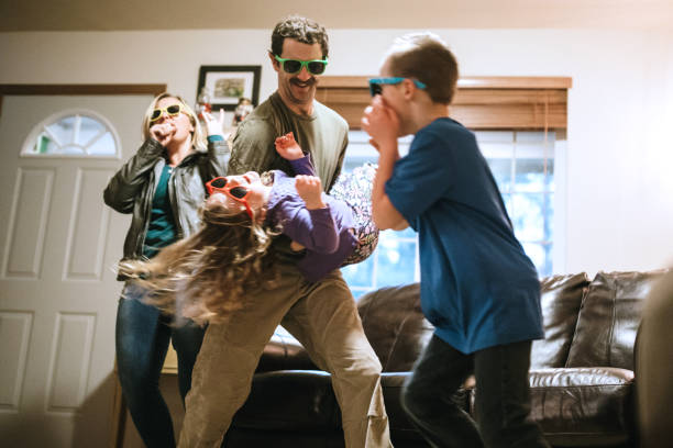 Family Dancing and Singing in Living Room A family has fun being silly and playful in their home, all of them wearing colored sunglasses while they lip synch to their favorite songs and dance around. dancing dad stock pictures, royalty-free photos & images