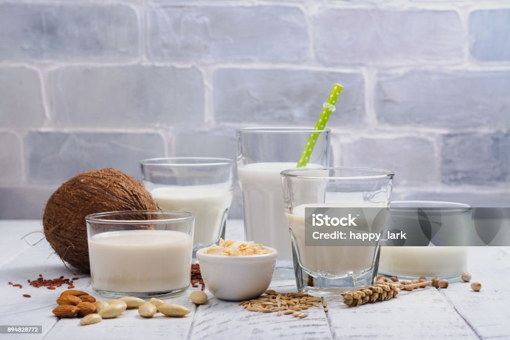 Assortment of non dairy vegan milk and ingredients Assortment of non dairy vegan milk and ingredients on white wooden background. Healthy drinks concept. Copy space Milk Stock Photo