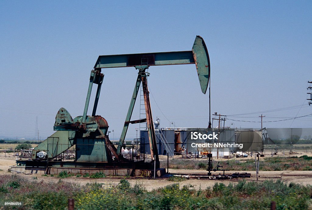 Bomba de aceite en un campo con tanques y cables en el fondo. - Foto de stock de Bomba de petróleo libre de derechos