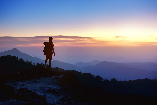 Silhouette of man with backpack at mountain top on background of sunset mountains