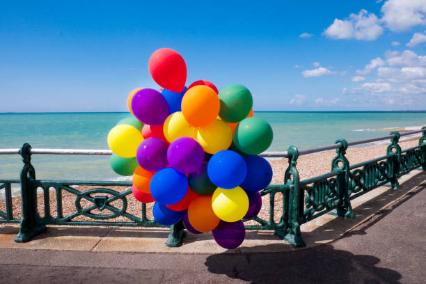 30 balloons on the beach 30 colorful balloons in a bunch hanginf of a railing on a sea front with the sea and blue sky behind, sunny day brighton england stock pictures, royalty-free photos & images