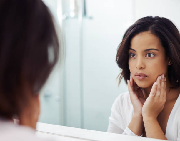 Who's the face staring back at you? Shot of an attractive young woman inspecting her face in the bathroom mirror during her morning beauty routine staring stock pictures, royalty-free photos & images