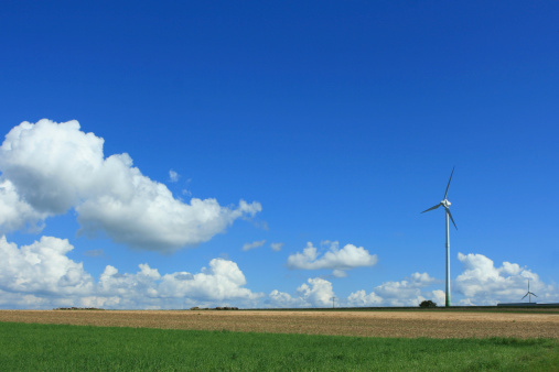 Wind turbine is standing in the beautiful summer landscape with green pasture and blue sky. This picture is taken in Luxembourg.