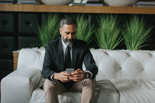 istock Middle-aged businessman using mobile phone in modern office on sofa 894994252