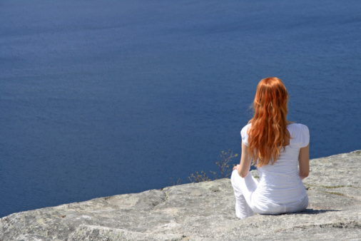Red-haired girl sitting on a rock and looking over blue water.