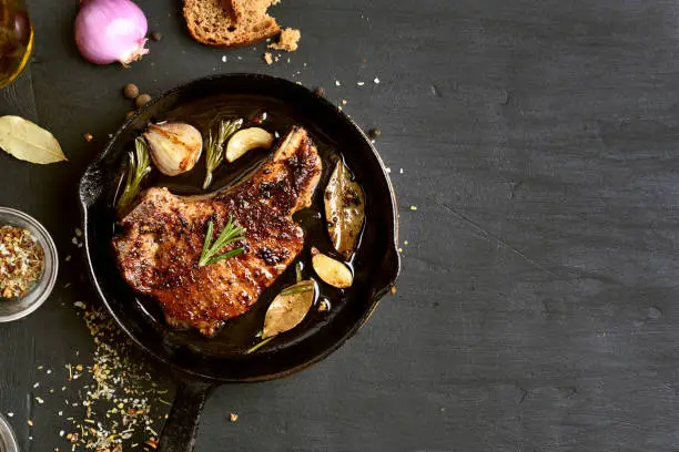 Grilled pork steak in frying pan on black background with copy space. Top view, flat lay food