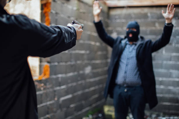 a man pointing a gun to another man whose face is covered with cap - gun handgun violence kidnapping imagens e fotografias de stock