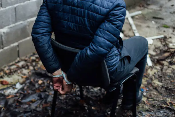 A man is sitting on a chair with his hands tied with a rope on his back.