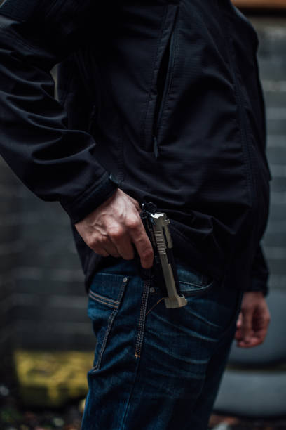 um homem com um casaco preto com uma arma na mão - gun handgun violence kidnapping - fotografias e filmes do acervo