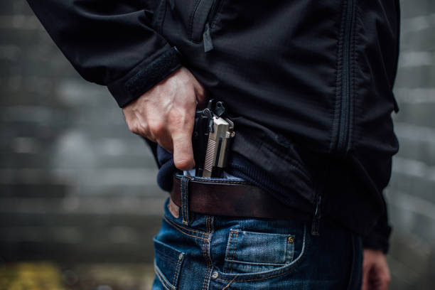 a mão do homem levando uma arma do bolso dele. - gun handgun violence kidnapping - fotografias e filmes do acervo